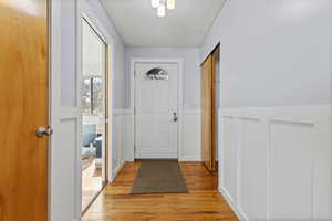 Doorway with wood finished floors, a textured ceiling, a wainscoted wall, and a decorative wall