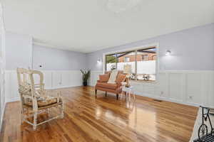 Living area with a decorative wall, wainscoting, wood finished floors, and a textured ceiling