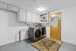 Washroom with a textured ceiling, washing machine and dryer, and cabinet space