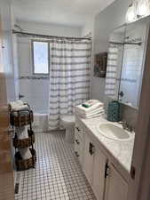 Bathroom featuring a textured ceiling, vanity, shower / tub combo with curtain, toilet, and tile patterned floors