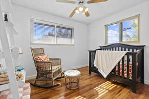 Bedroom with a nursery area, light wood finished floors, a textured ceiling, and ceiling fan