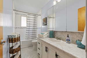 Full bathroom with shower / bath combination with curtain, vanity, a textured ceiling, light tile patterned floors, and backsplash