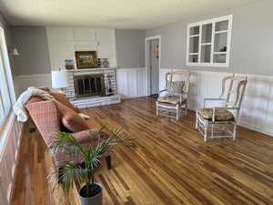 Living area with a textured ceiling, wood finished floors, a wainscoted wall, a decorative wall, and a stone fireplace
