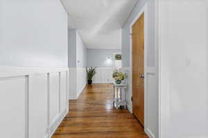 Hall with wainscoting, hardwood / wood-style floors, a textured ceiling, and a decorative wall