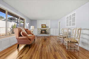 Sitting room with a decorative wall, wainscoting, a textured ceiling, a stone fireplace, and light wood-style floors