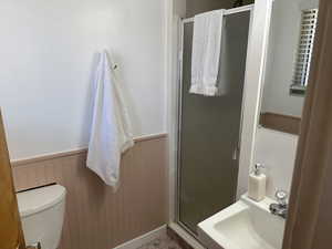 Bathroom featuring wainscoting, a shower stall, toilet, and a sink