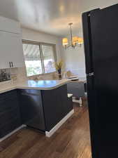 Kitchen featuring freestanding refrigerator, stainless steel dishwasher, white cabinetry, dark wood-style floors, and a peninsula