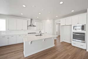 Kitchen featuring oven, built in microwave, white cabinets, wall chimney exhaust hood, and a sink