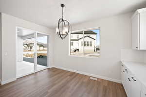 Unfurnished dining area featuring an inviting chandelier, plenty of natural light, light wood-style floors, and visible vents