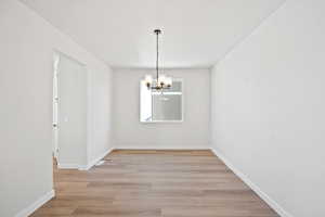 Unfurnished dining area featuring light wood-style flooring, a notable chandelier, and baseboards