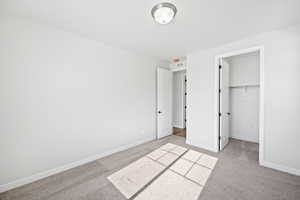 Unfurnished bedroom with baseboards, light carpet, visible vents, and a walk in closet