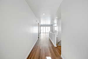Hallway featuring wood finished floors, baseboards, recessed lighting, a textured ceiling, and an upstairs landing