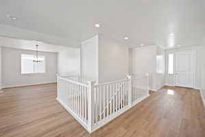 Interior space featuring light wood finished floors, baseboards, a chandelier, an upstairs landing, and recessed lighting