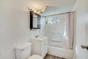 Bathroom with toilet, shower / bath combo with shower curtain, wood finished floors, a textured ceiling, and vanity