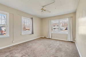 Carpeted spare room with visible vents, baseboards, and a ceiling fan