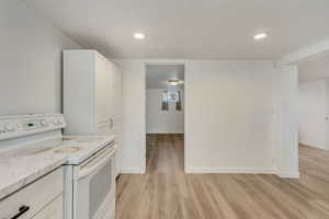 Kitchen featuring white range with electric cooktop, light wood-style flooring, white cabinetry, and baseboards