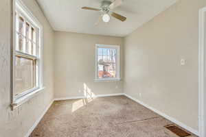 Carpeted spare room featuring baseboards, visible vents, a textured wall, and ceiling fan