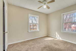 Carpeted spare room with ceiling fan, baseboards, and a textured wall