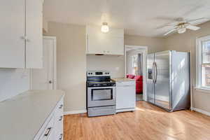 Kitchen with baseboards, light countertops, light wood-style flooring, white cabinets, and stainless steel appliances