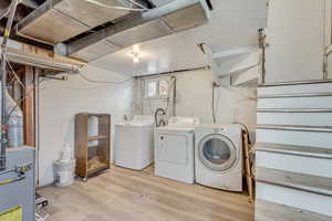 Clothes washing area with laundry area, light wood-style flooring, separate washer and dryer, and a heating unit