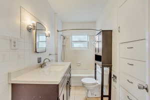 Full bathroom featuring toilet, vanity, bathtub / shower combination, tile patterned floors, and tile walls