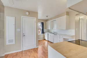 Kitchen with a sink, white cabinetry, light wood-style floors, light countertops, and dishwasher