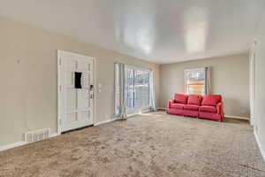 Carpeted living room with visible vents and baseboards