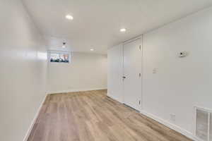 Below grade area with light wood-style floors, recessed lighting, baseboards, and visible vents