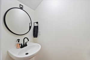 Bathroom with a textured ceiling, vaulted ceiling, and a sink