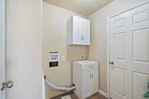 Clothes washing area with a textured ceiling, hookup for a washing machine, cabinet space, and electric dryer hookup