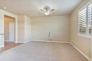 Empty room with ceiling fan, a textured ceiling, baseboards, and carpet floors