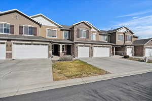 View of property featuring a garage, stone siding, driveway, and stucco siding