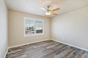 Empty room with wood finished floors, baseboards, visible vents, ceiling fan, and a textured ceiling