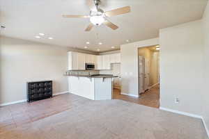 Kitchen with light carpet, stainless steel microwave, a kitchen breakfast bar, a peninsula, and light tile patterned floors