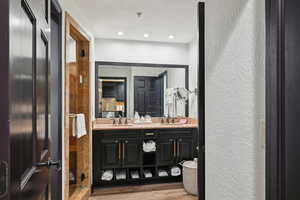 Full bath with a sink, wood finished floors, double vanity, and a textured wall