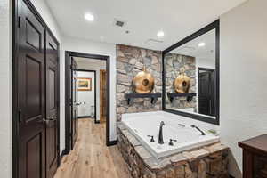 Bathroom featuring visible vents, a garden tub, wood finished floors, recessed lighting, and a textured wall