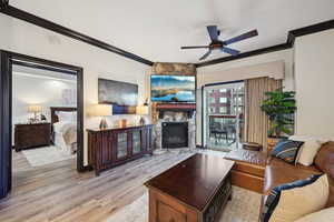 Living area with a fireplace, ceiling fan, wood finished floors, and ornamental molding