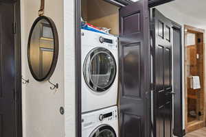 Washroom with laundry area, a textured wall, and stacked washer / drying machine