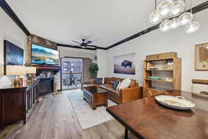 Dining area featuring a ceiling fan, a stone fireplace, wood finished floors, and crown molding