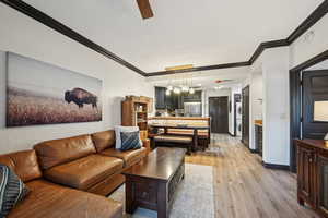 Living area featuring light wood-style flooring, stacked washing maching and dryer, baseboards, and ornamental molding