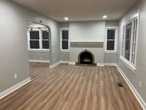 Unfurnished living room with arched walkways, visible vents, a brick fireplace, wood finished floors, and baseboards