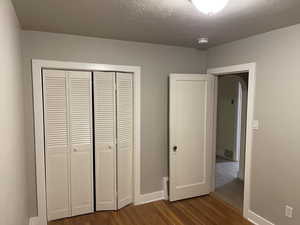 Unfurnished bedroom featuring a textured ceiling, a closet, baseboards, and dark wood-type flooring