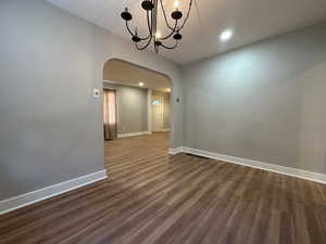 Unfurnished dining area with arched walkways, a chandelier, recessed lighting, baseboards, and dark wood finished floors