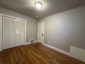 Unfurnished bedroom featuring dark wood-style flooring, visible vents, and baseboards