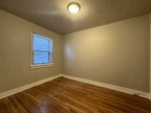 Empty room with dark wood-style flooring, a textured ceiling, and baseboards