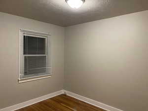 Empty room with dark wood-style floors, baseboards, and a textured ceiling
