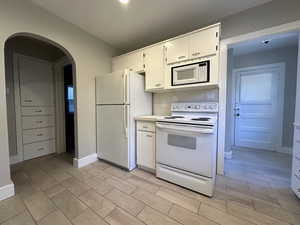 Kitchen featuring arched walkways, light countertops, wood tiled floor, white cabinetry, and white appliances