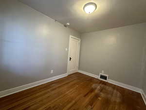 Unfurnished room featuring dark wood-style flooring, visible vents, and baseboards