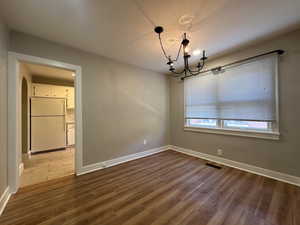 Unfurnished dining area with arched walkways, a notable chandelier, wood finished floors, visible vents, and baseboards
