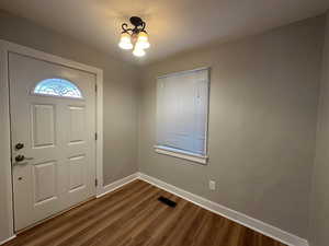 Foyer with dark wood-style floors, a notable chandelier, visible vents, and baseboards